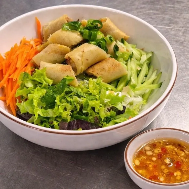 Bún Chả Giò Chay at Bà Năm Adelaide — white ceramic bowl of rice vermicelli topped with whole golden vegetarian fried spring rolls and spring onion, shredded carrot on the left, julienned cucumber on the right, lettuce, mint and purple leaf at the front, with a small side bowl of dipping sauce with chilli, garlic and crushed peanut.