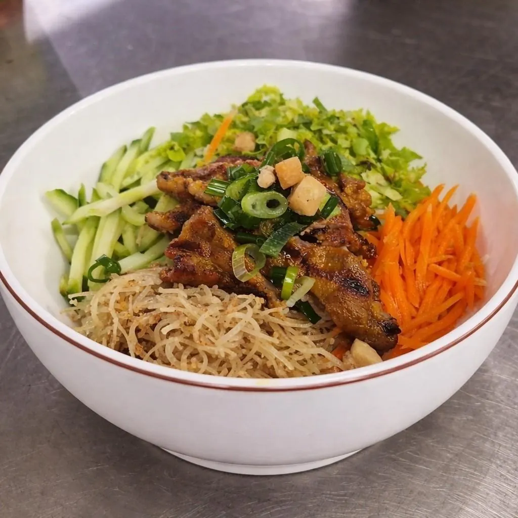 Bún thịt nướng at Bà Năm Adelaide: white ceramic bowl with caramelised char-grilled pork slices in the centre, surrounded by shredded cucumber, lettuce and herbs, bright shredded carrot and thin rice vermicelli, topped with spring onion and golden fried shallots.