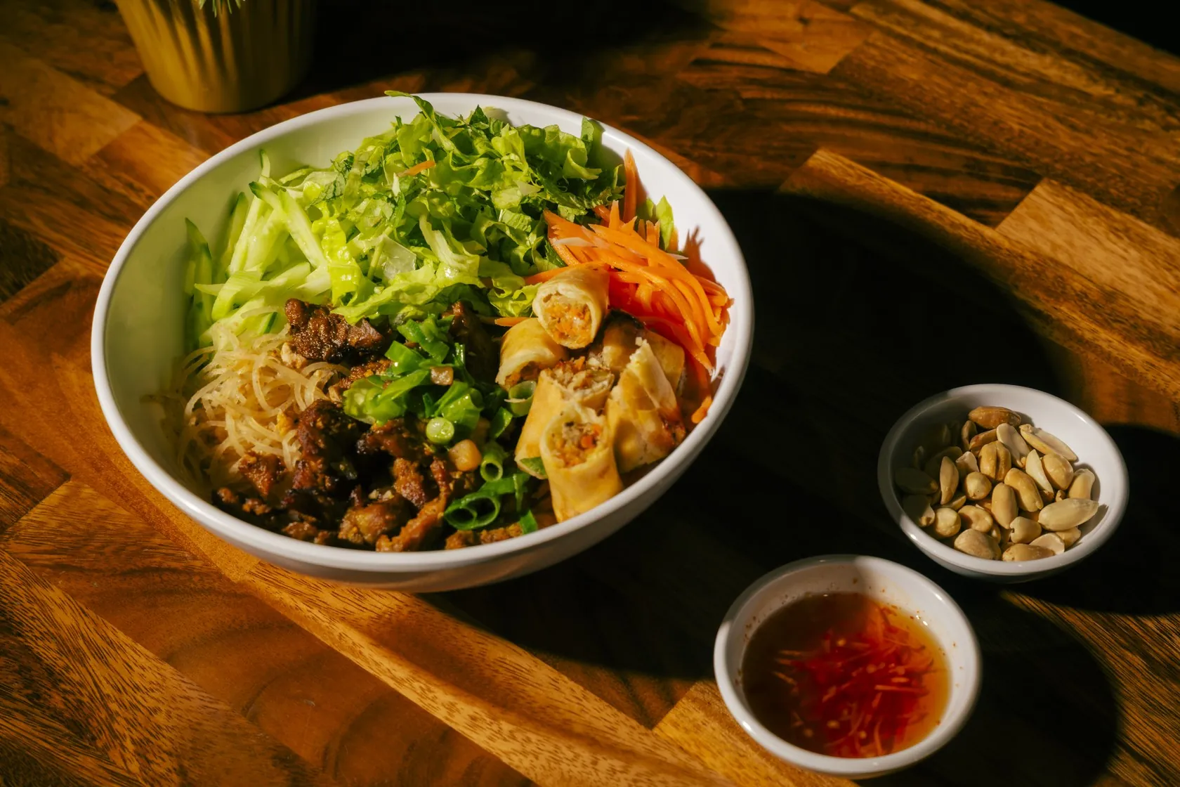 Vermicelli bowl at Bà Năm Restaurant, Adelaide, topped with sliced chả giò, fresh herbs, carrot and cucumber, with nước chấm and crushed peanuts on the side