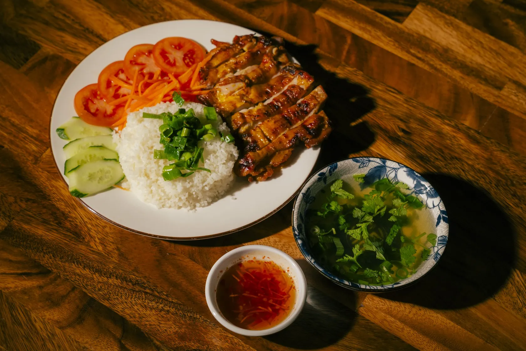 Cơm Gà Nướng at Bà Năm Adelaide — sliced char-grilled chicken with grill marks, white rice topped with spring onion, tomato, cucumber, shredded carrot, clear soup and chilli nước chấm