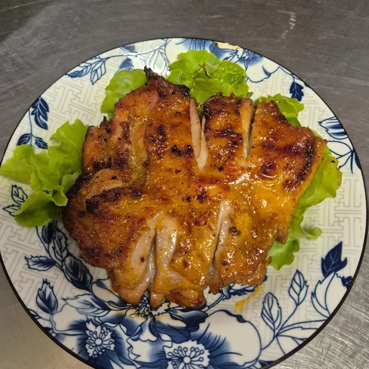 Sliced char-grilled Gà Nướng chicken thigh with caramelised glaze and grill marks, served on green lettuce on a blue-and-white floral plate at Bà Năm, Adelaide