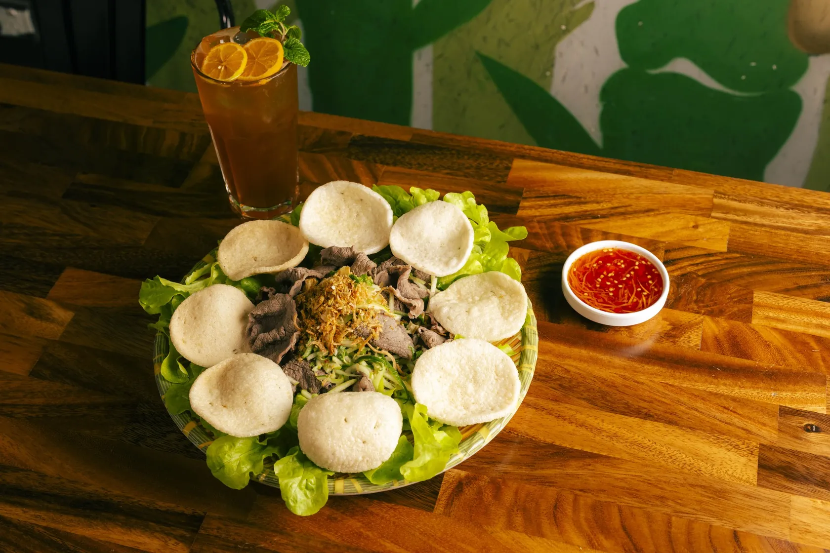 Gỏi bò tái chanh lime-cured rare beef salad ringed with prawn crackers, iced tea with lime and chilli sauce on a timber table at Bà Năm, 65 Grote Street Adelaide