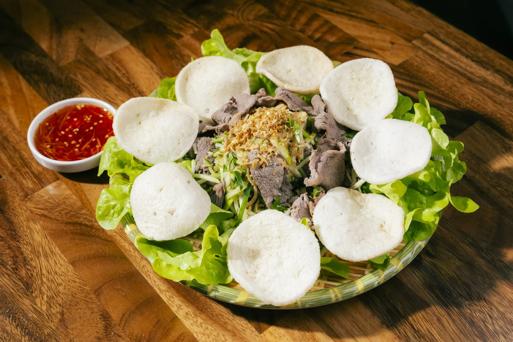 Gỏi bò tái chanh on a bamboo tray with prawn crackers, fresh lettuce and nước chấm, served on a timber table at Bà Năm, Grote Street Adelaide