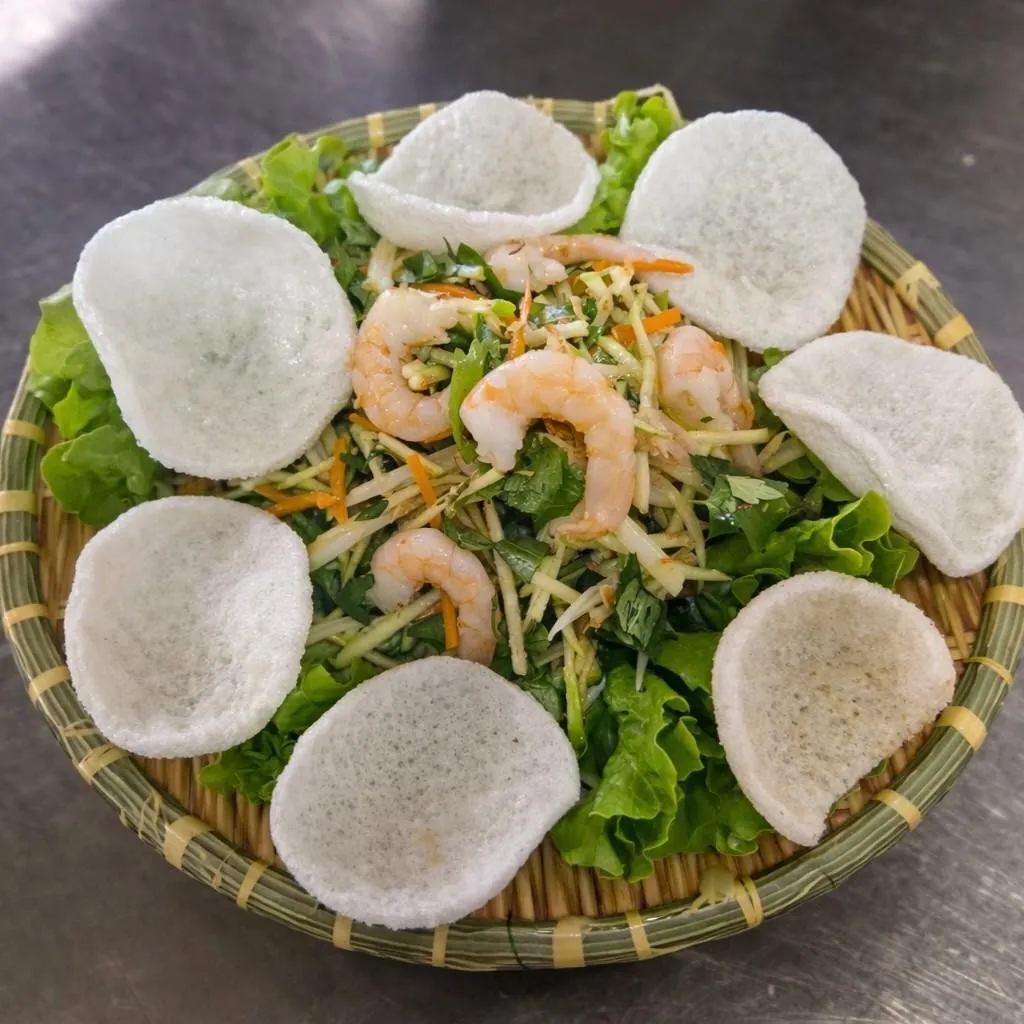 Gỏi ngó sen tôm thịt at Bà Năm Adelaide — shredded lotus root, carrot and herbs topped with prawns, ringed by prawn crackers on lettuce in a bamboo basket.