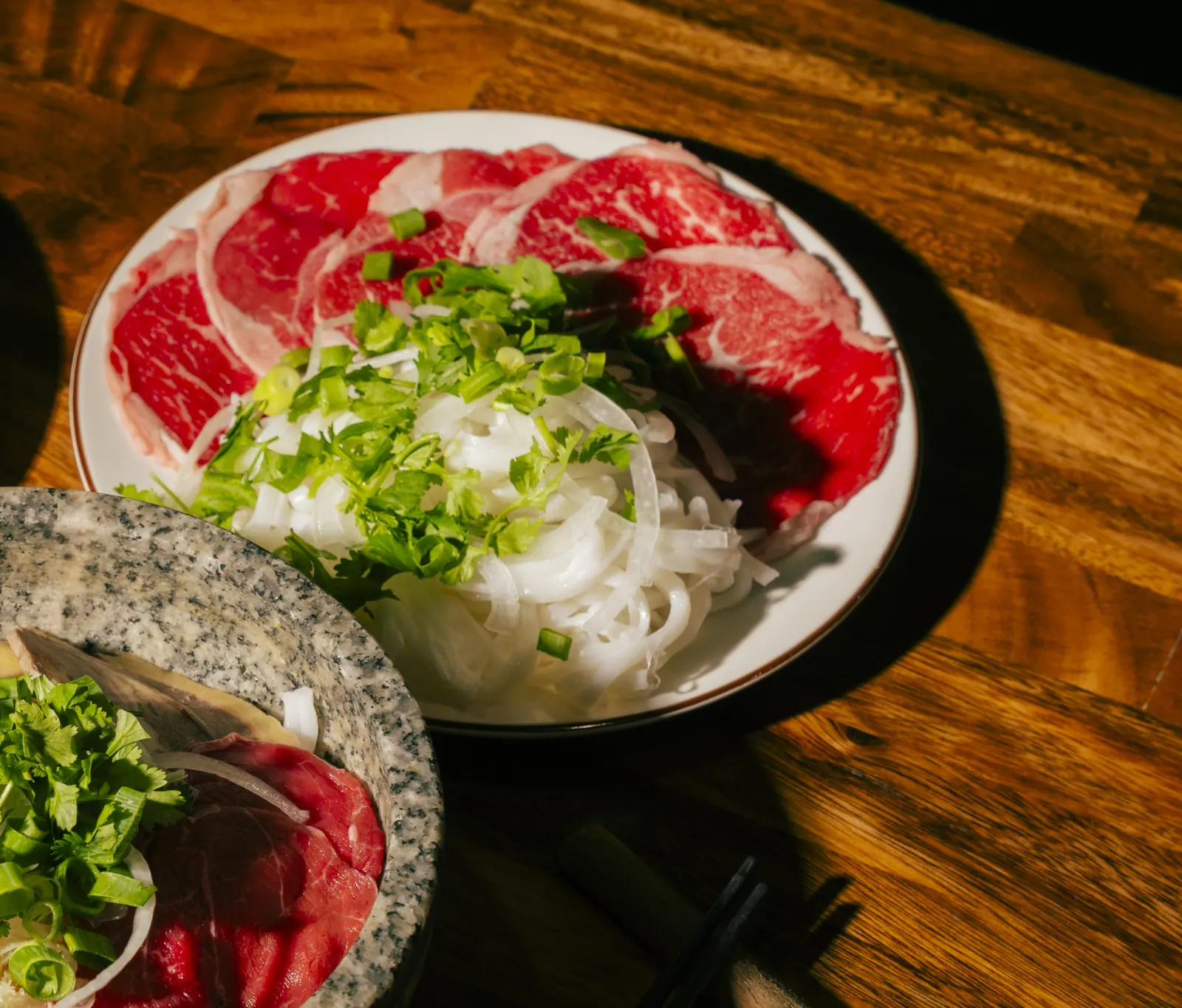 Platter of paper-thin round rare beef slices with onion and coriander, ready for Phở Tái at Bà Năm