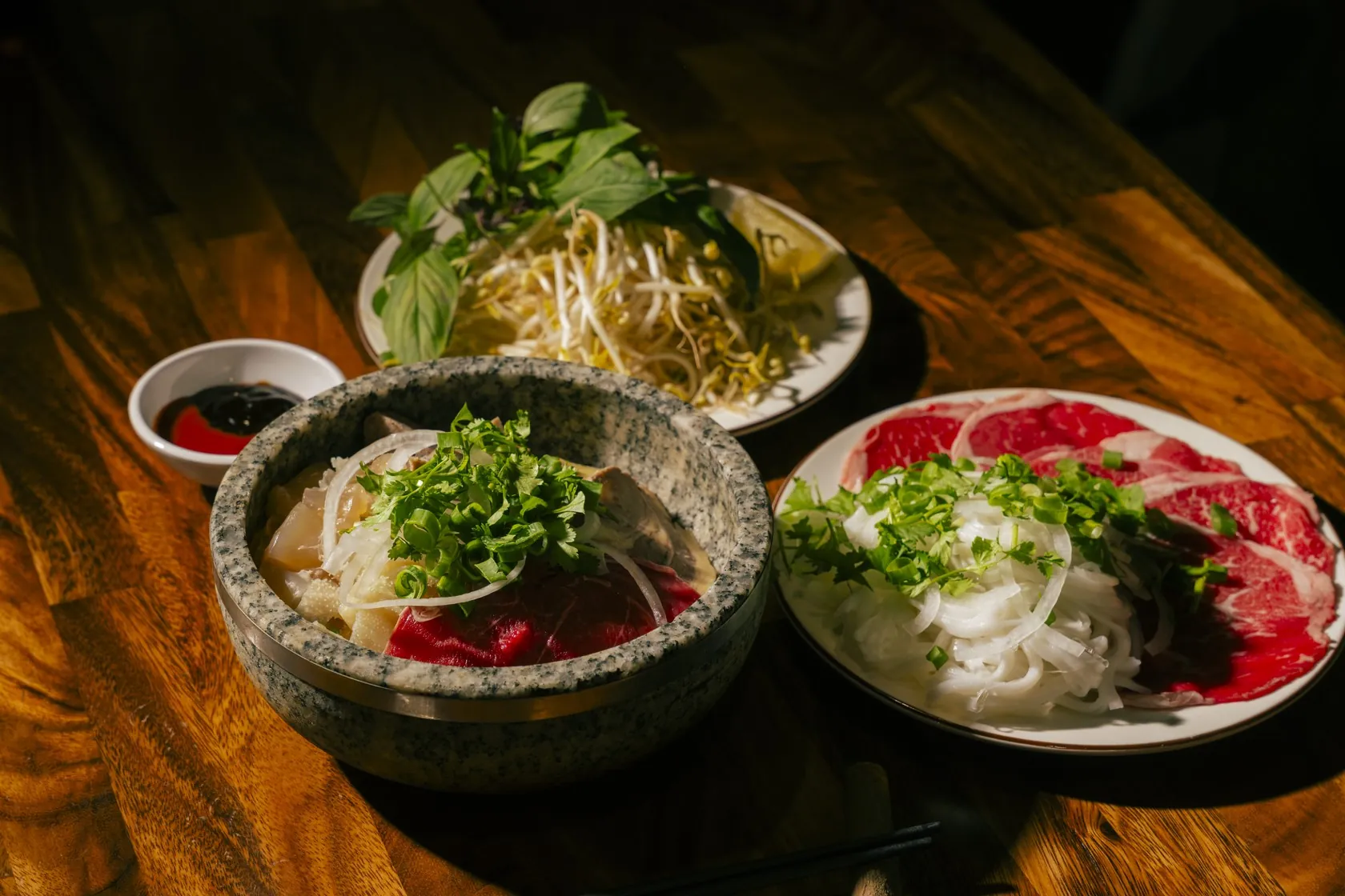 Stone-bowl phở with rare beef, noodles and a herb plate at Bà Năm Restaurant, Adelaide — the red-coin Phở Tái set