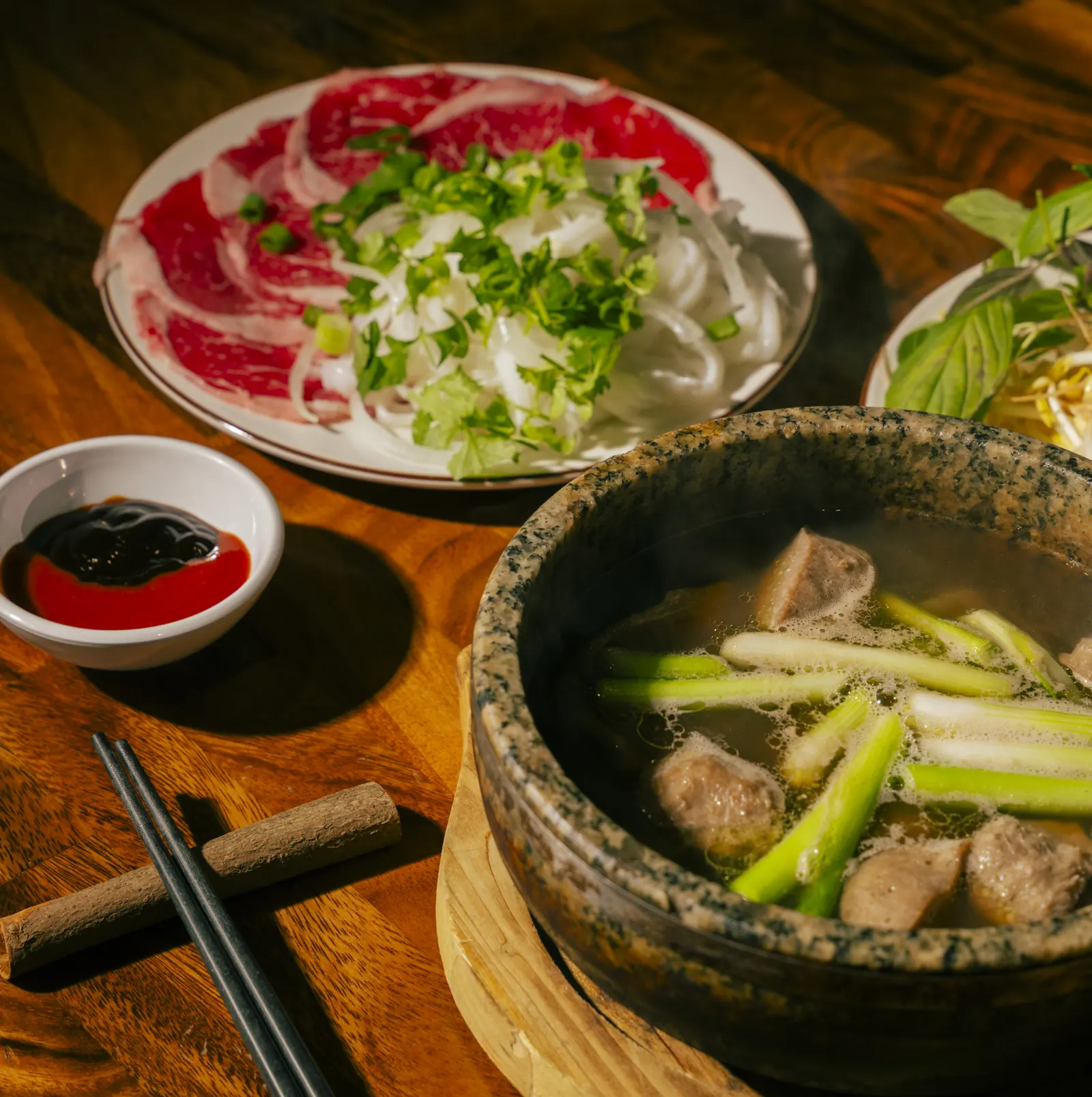 Steaming stone bowl of phở broth beside a plate of paper-thin raw beef at Bà Năm, Adelaide
