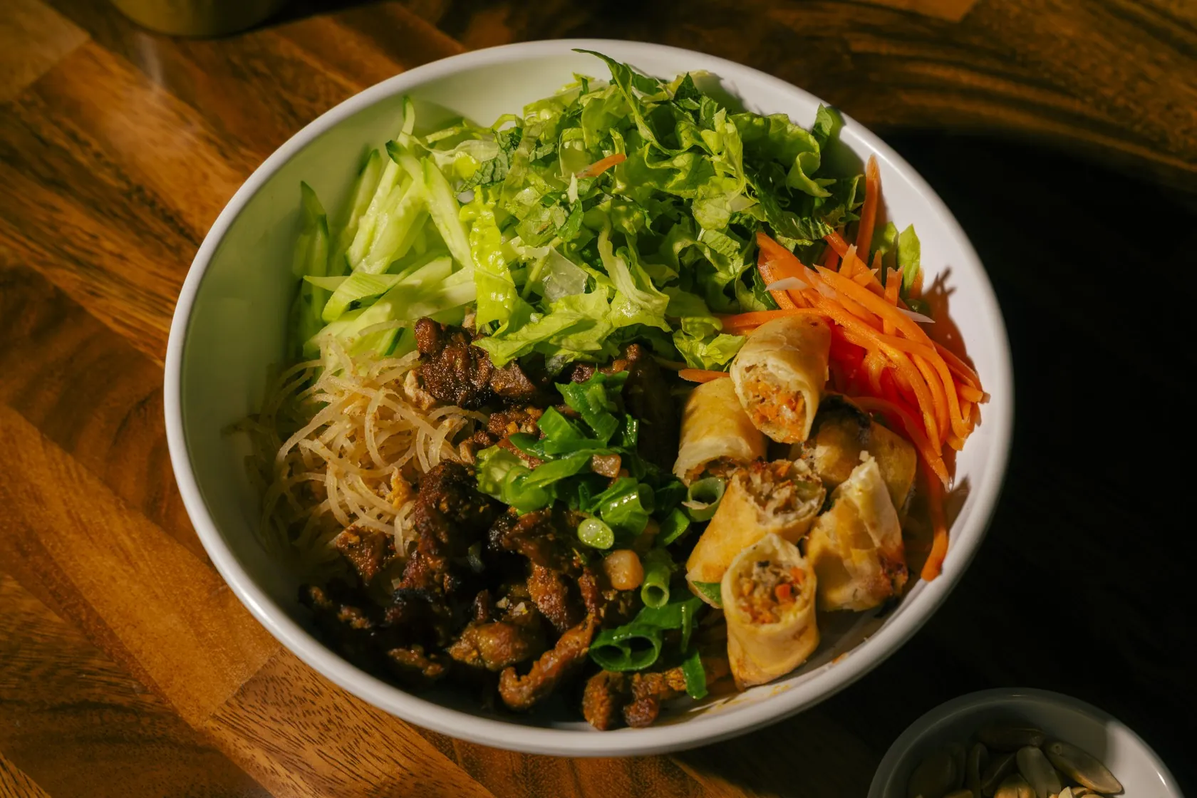 A shared Vietnamese vermicelli bowl with spring rolls, herbs and fresh vegetables at Bà Năm Restaurant, Adelaide — the hands-on, wrap-and-dunk side of the table that bánh xèo belongs to