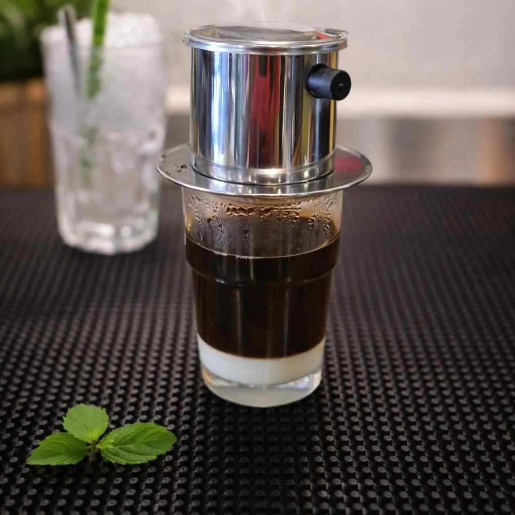 Cà phê sữa đá at Bà Năm — phin filter dripping dark robusta over sweet condensed milk in a chilled glass, mint sprig in front.