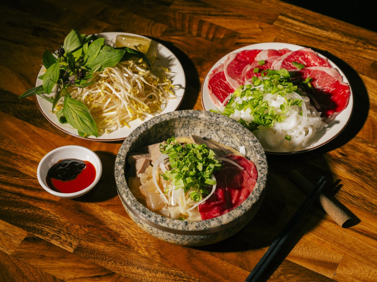 A Bà Năm phở spread — stone-bowl pho with rare beef, fresh herbs and bean sprouts