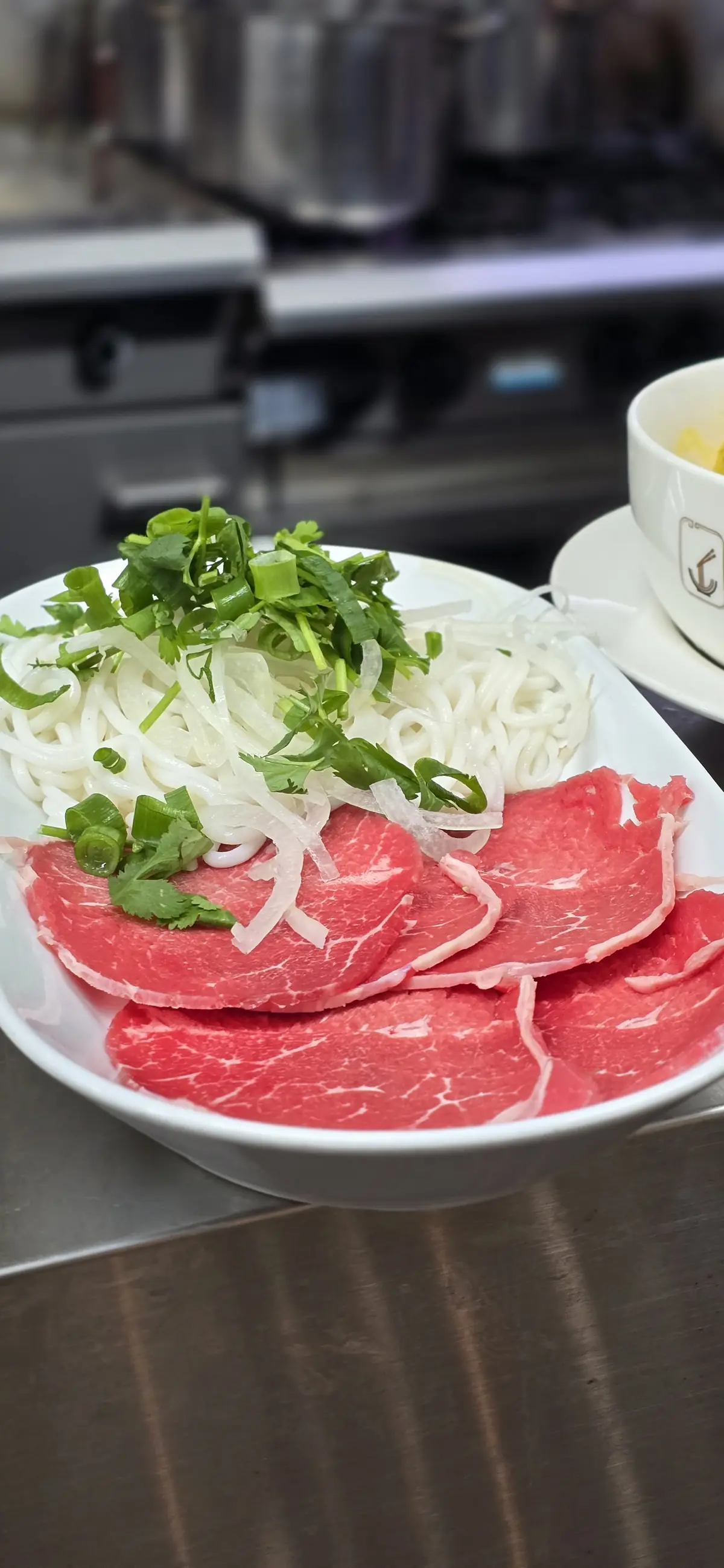 Step one — raw marbled beef slices laid by hand beside rice noodles and fresh herbs